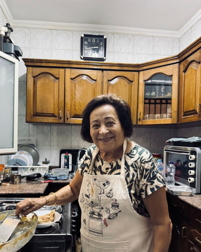 A grandmother cooking in her kitchen, wearing the Making Molokheya apron