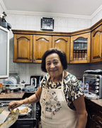 A grandmother cooking in her kitchen, wearing the Making Molokheya apron