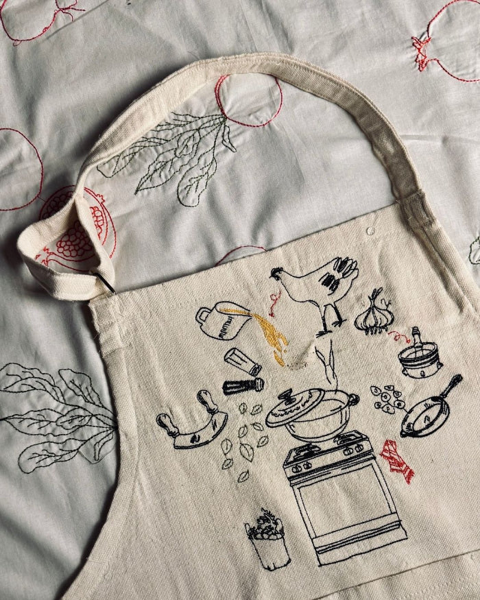 Cream Making Molokheya apron with a hand-illustrated pot, pan and kitchen scene, laid flat