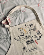 Cream Making Molokheya apron with a hand-illustrated pot, pan and kitchen scene, laid flat