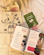 Open Egyptian cookbook and a greeting card beside a cream apron with a hand-drawn molokheya cooking illustration
